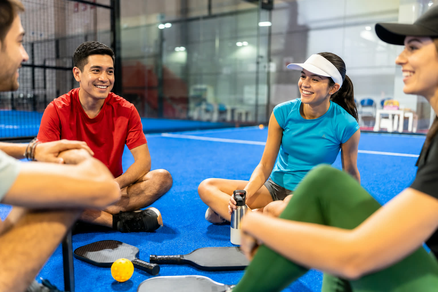Friends laughing courtside with paddles and a pickleball between them